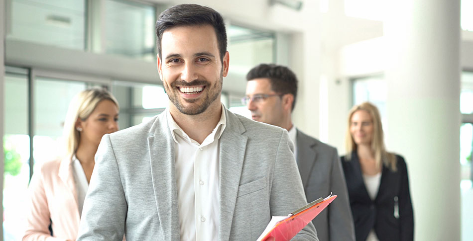 Man smiles at camera while holding a clipboard.