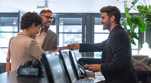 People at a hotel counter handing documents over to a staff member behind the counter.