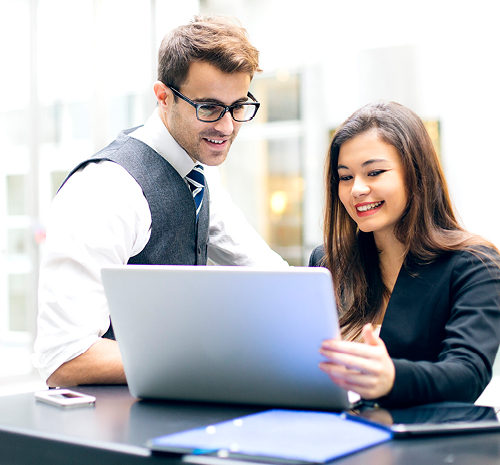 2 people looking at a laptop screen sitting on a table in front of them