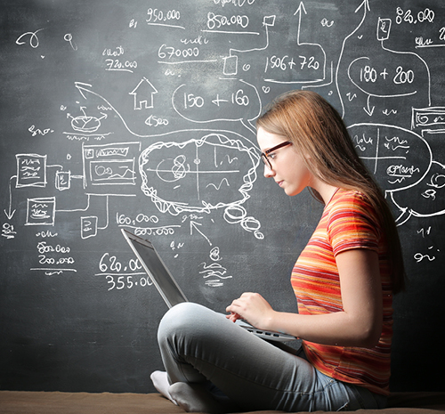 Person sitting in front of a chalkboard cross legged with a laptop open on their lap