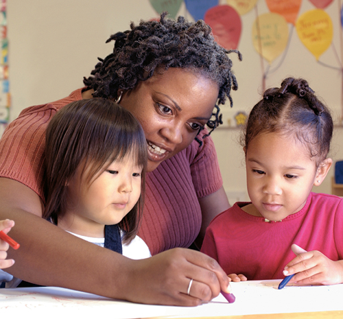 teacher working with 2 young children coloring on paper with crayons
