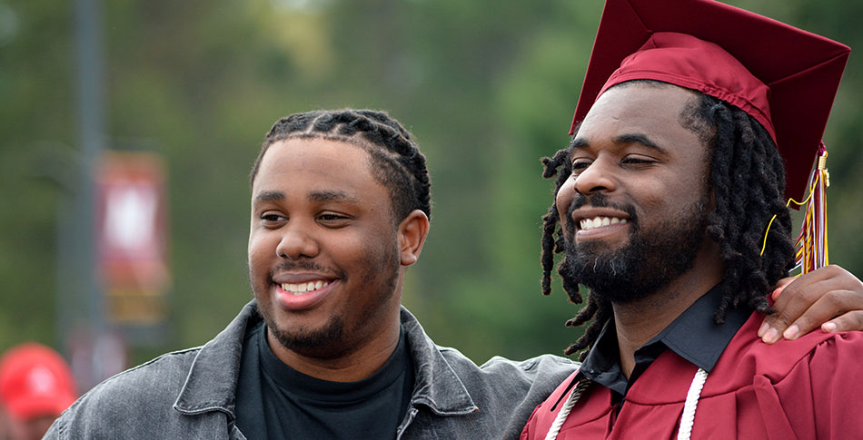 Mid-State graduate in cap and gown on graduation day stands next to family member.