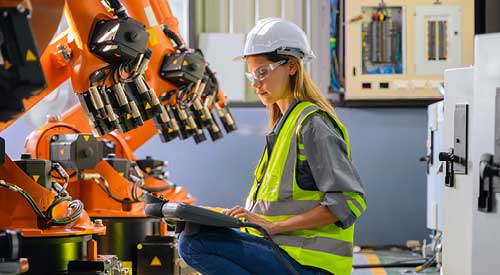 Person squatting down next to machinery looking down at a tablet