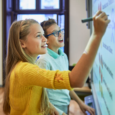 Two elementary-aged students at a white board, one of them writing