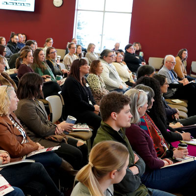 An audience sits in chairs with attention on the speaker in front of them