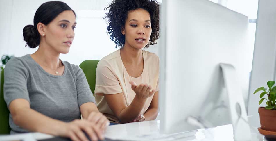 2 people sitting at a desk looking at a computer monitor