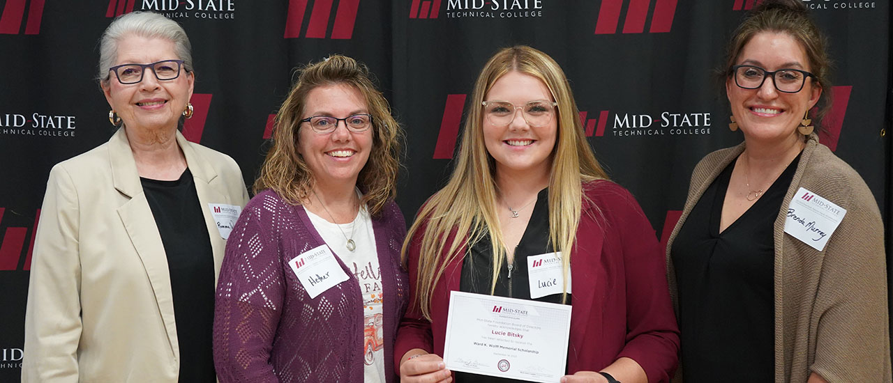 Three women donors stand next to scholarship recipient Lucie Bitsky, who is holding a paper representing her scholarship.