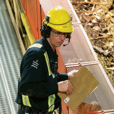 Person in Domtar attire wearing a yellow safety helmet and a headset holding a clipboard