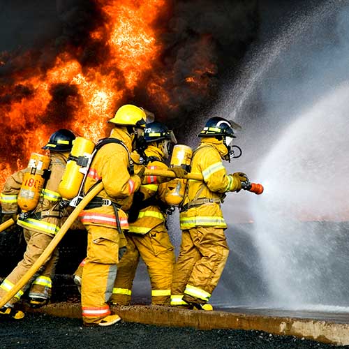 A group of firefighters holding a hose that is spraying water on a fire
