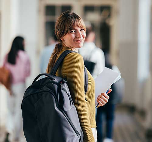 College student looking over her shoulder wearing a backpack.