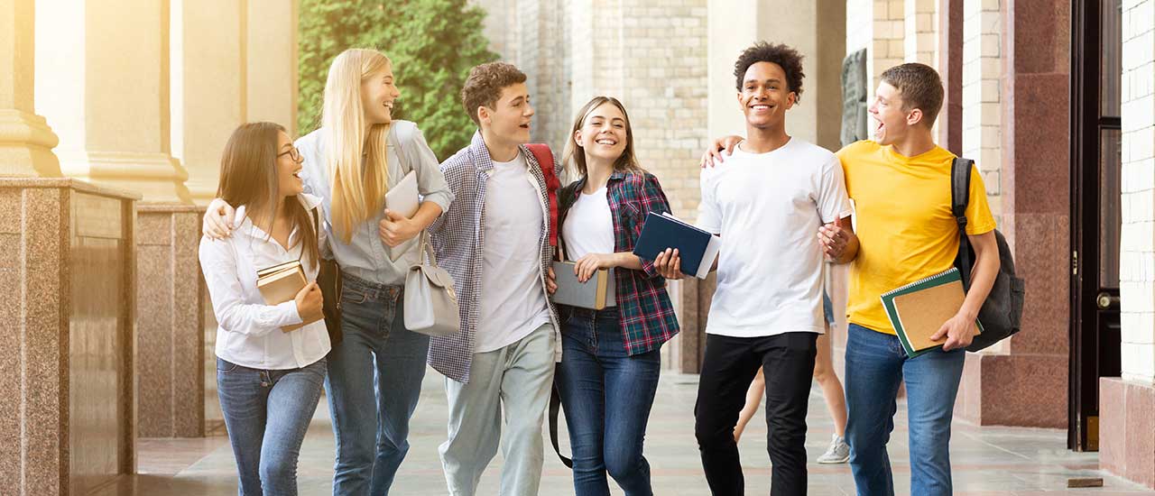 Group of teenagers walking in a line holding school supplies.