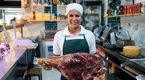 Person holding a large piece of meat in an industrial kitchen, smiling at the camera