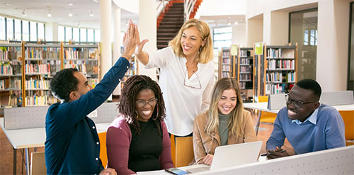People sitting and standing by a table. Two people are high fiving each other.