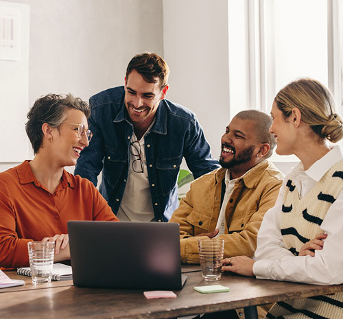 4 People sitting around a laptop smiling at each other