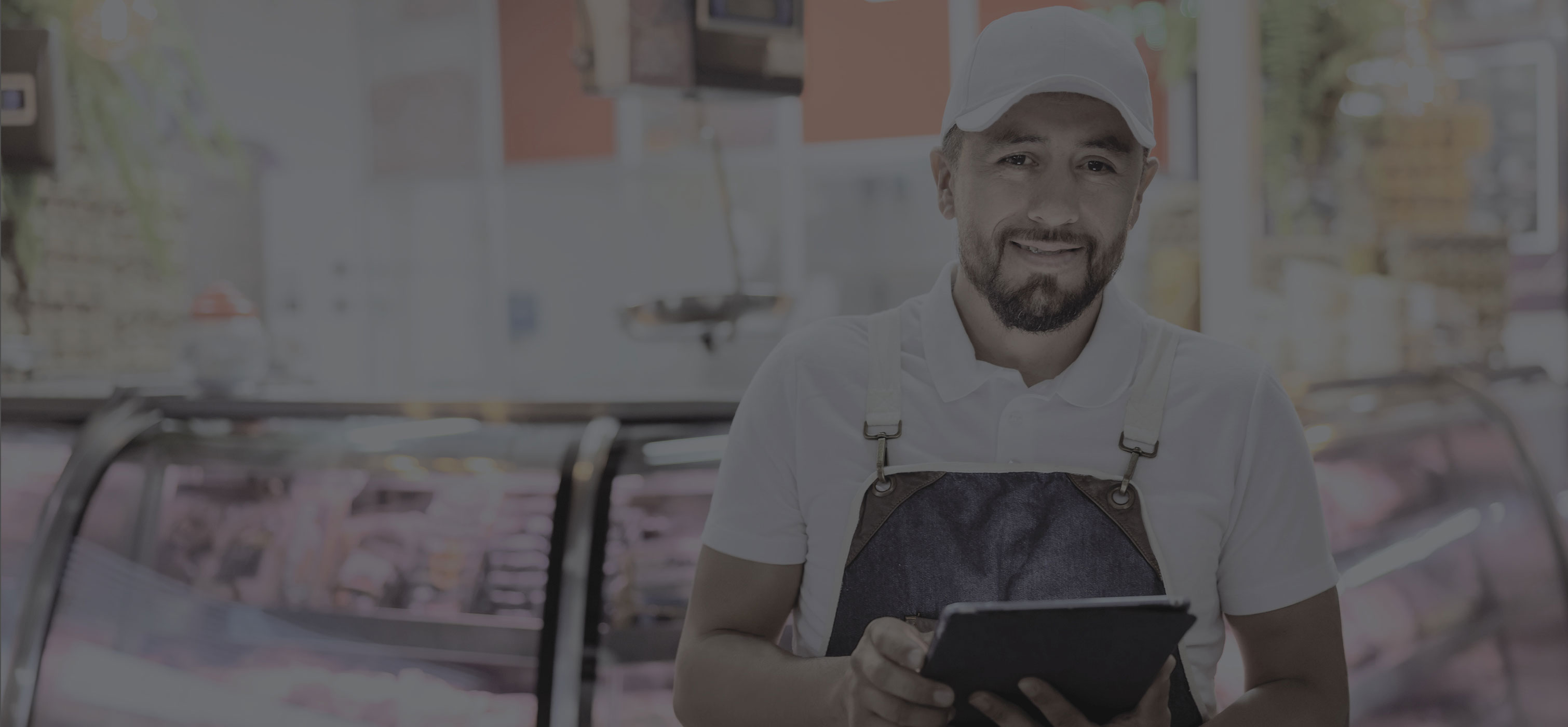 Person in an apron holding a tablet standing in front of a meat counter