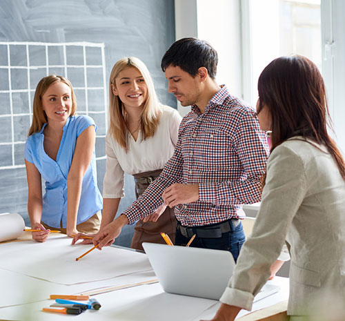 4 people standing around a table with large sheets of paper and writing utencils.