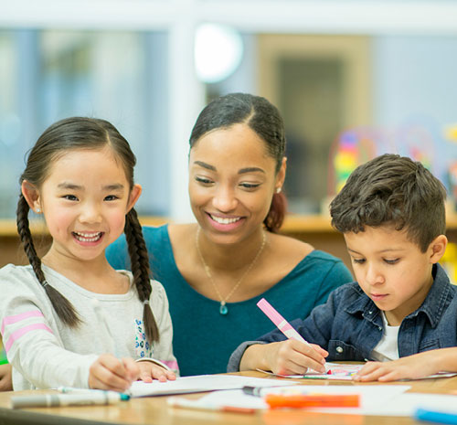 Teacher working with 2 children coloring sitting at a desk