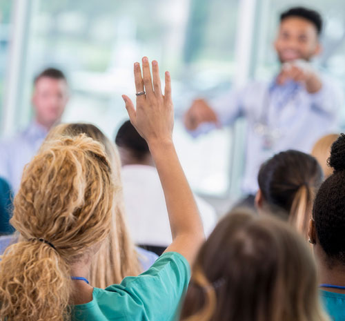 Person presenting to a crowd pointing to a person in the crowd who has their hand up