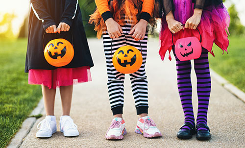 3 kids holding pumpkin buckets dressed up for trick or treating