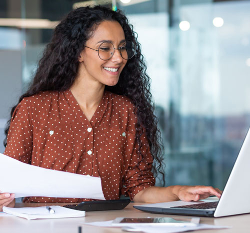 Person sitting in front of a laptop holding a sheet of paper smiling