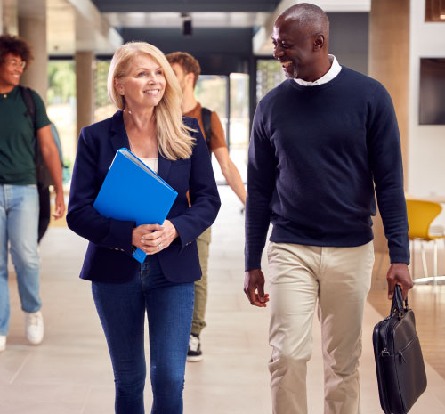Two people walking in front of 2 students walking down a hallway