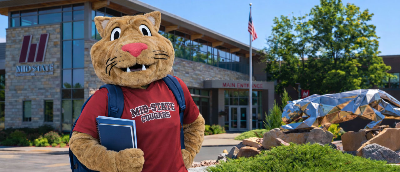 Mid-State Mascot Grit standing in front of the Wisconsin Rapids Campus building