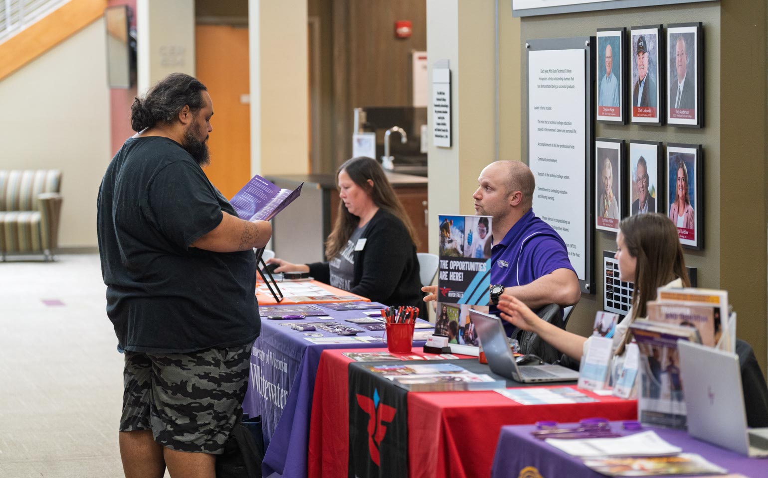 Transfer fair participant speaks with college representatives at a booth.