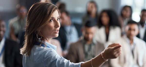 Person pointing to their right while presenting to a crowd of people in their seats.