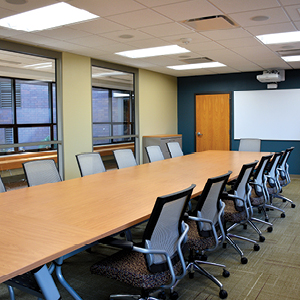 Long conference table with 13 chairs in view around it whiteboard with projector mounted at head of room