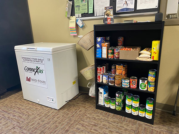 Adams Campus Food Pantry. Shelving with canned and boxed goods, and a mini freezer