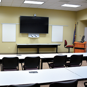 Training Room with multiple chairs at desks and tv mounted in front of room with a computer at a podium