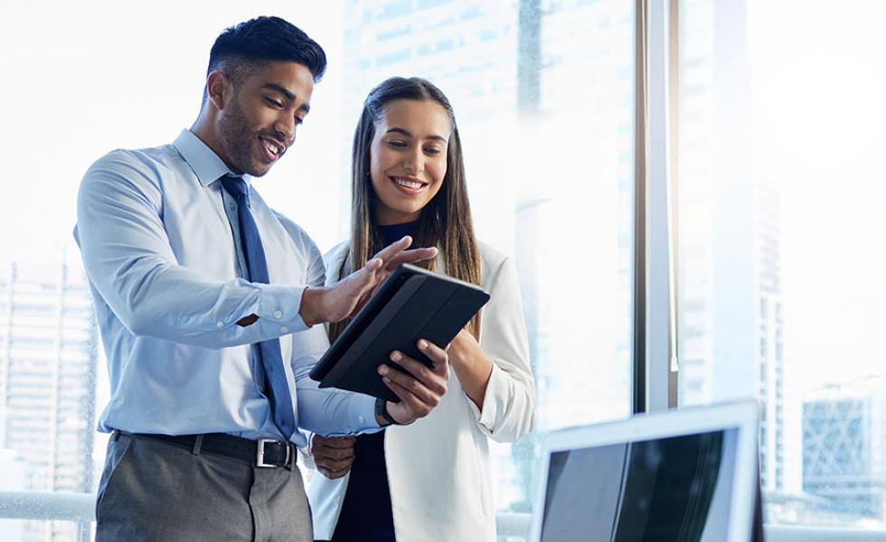 Two people in business professional attire look at an electronic device.