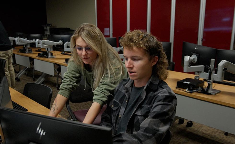Natasha Janicki looks over the shoulder of her classmate as the two look at a computer screen.