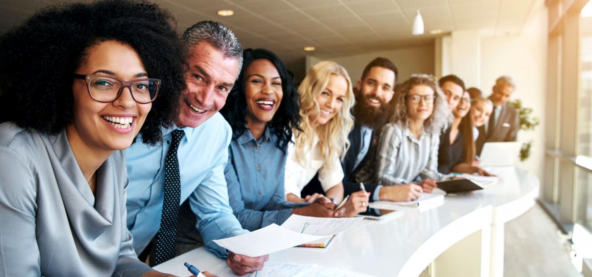 People leaning over a long conference table, dressed in business attire, looking toward the camera