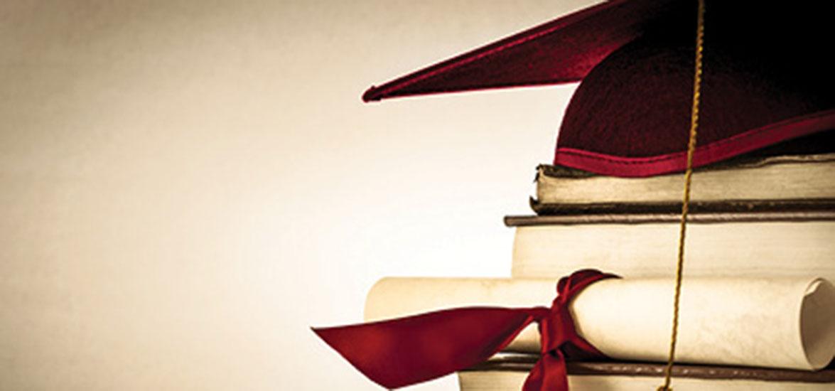 Graduation cap on top of pile of books with rolled up diploma sitting in front.