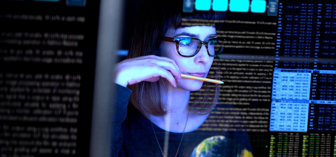Female IT professional holding a pencil looks at a computer monitor displaying code and images