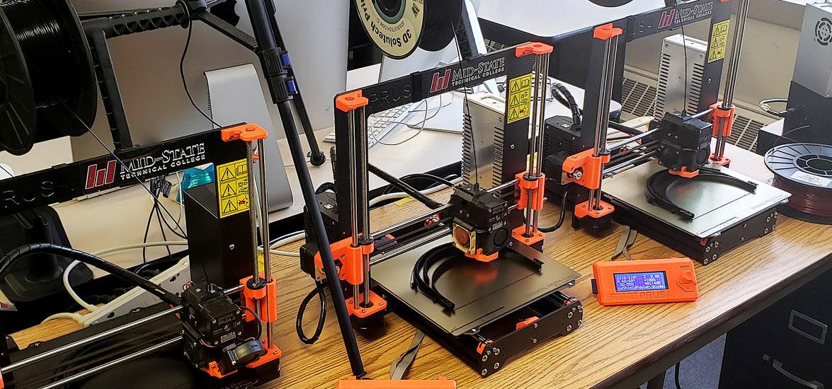 Mid-State Technical College 3D printers in their temporary location in the IDEA Center of CREATE Portage County, where they join other printers on loan from the community to produce reusable face masks and face shields for local hospitals and clinics in need.