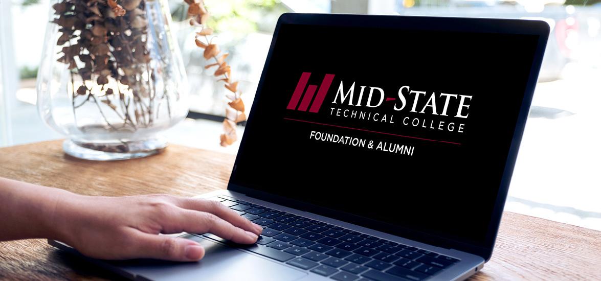 A laptop sitting on a desk with a hand resting on the keypad. The screen shows the logo for the Mid-State Technical College Foundation & Alumni.