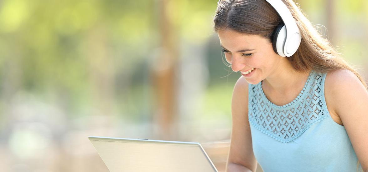 Smiling female student works on her laptop while wearing headphones