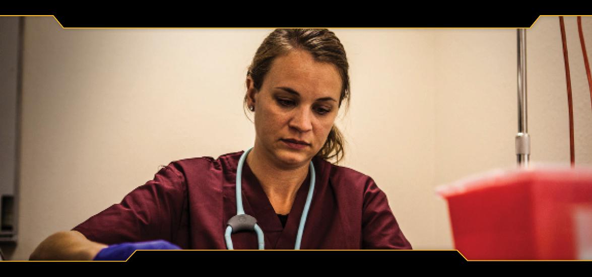 Female nursing student with stethoscope and gloved hands practices intravenous administration on simulator arm