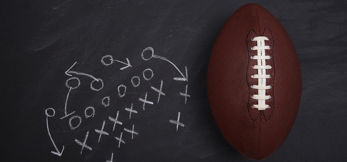 Xs and Os drawn in chalk on a blackboard in the form of a football play. A football is next to the drawing.