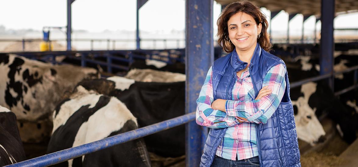 Woman standing with her arms crossed inside of an enclosure next to cows.