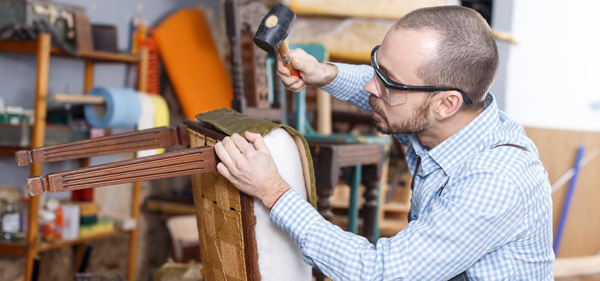 A man wearing safety glasses hammers fabric onto a chair.