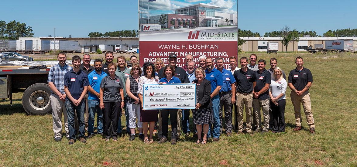Donaldson Stevens Point Plant Manager Lori Schlueter, front and center, presents Dr. Bobbi Damrow, Mid-State vice president of Workforce Development & Community Relations, left, and Dr. Shelly Mondeik with Donaldson’s $100,000 check during Mid-State’s AMETA Center site dedication in Stevens Point, July 22. Also pictured are AMETA Center campaign co-chair Wayne Bushman, (behind Schlueter) as well as Mid-State faculty and staff and Donaldson staff. (Photo by Jessica Kopecky Design)