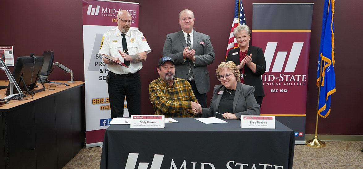 Adams Fire District Board of Directors President Randy Theisen, seated left, and Mid-State President Dr. Shelly Mondeik sign a ten-year partnership agreement between the organizations to create a fire training site in Adams. Standing, from left, are Adams Fire Chief Darin Kurth, Mid-State Associate Dean of Protective & Human Services Rick Anderson and Mid-State Adams Campus Dean Laurie Inda.