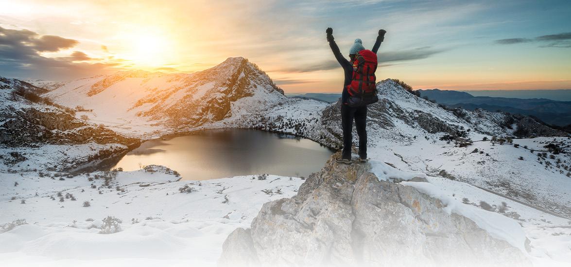 Person on snowy mountains with hands in the air overlooking a lake below.
