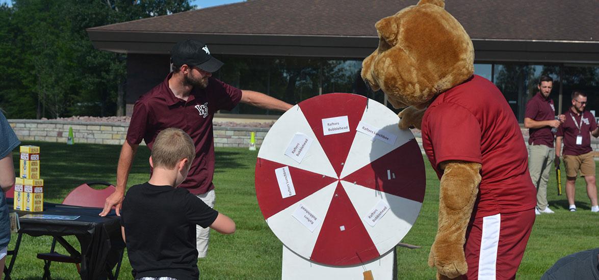 A 2022 Rafters Meet-and-Greet attendee spins the prize wheel with Grit, Mid-State’s mascot, and a Wisconsin Rapids Rafters staff member.
