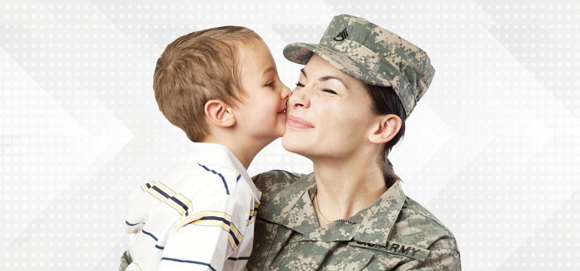 Mother dressed in military uniform receives kiss on the cheek from her young son.