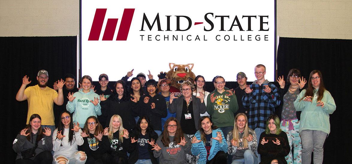 Admit Day attendees surround Mid-State’s mascot, Grit, and Mid-State President Dr. Shelly Mondeik while showing their Mid-State pride by holding up cougar paws, at the May 2023 Admit Day celebration on the Wisconsin Rapids Campus.