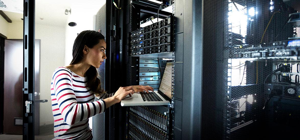 IT Security Specialist works on a laptop in a server room.